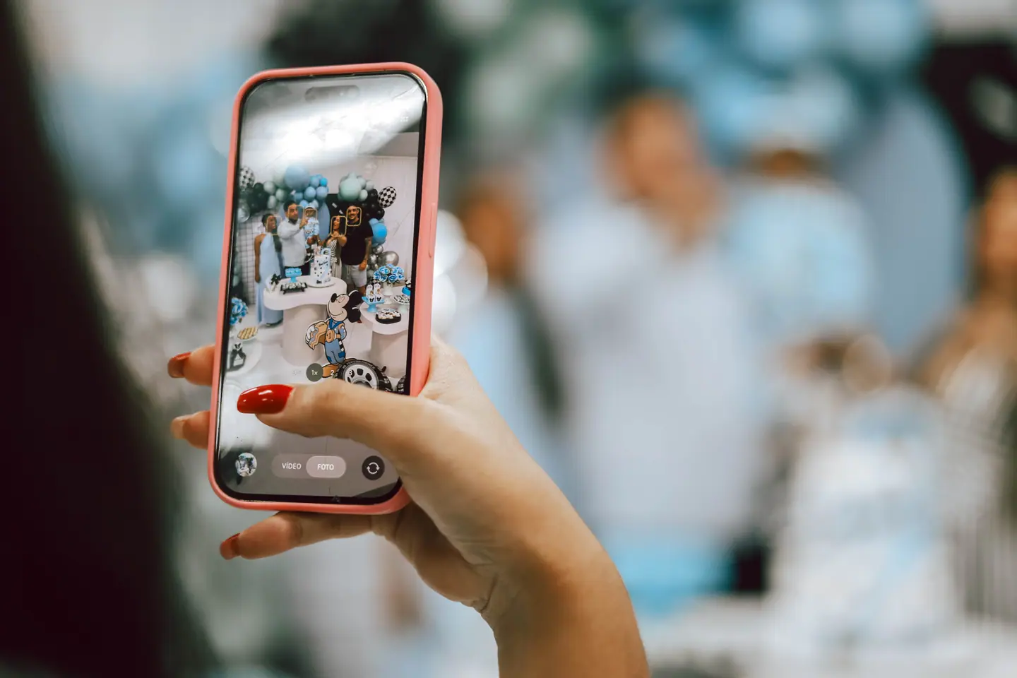 Convidada fotografa a festa com o celular, com a decoração desfocada ao fundo