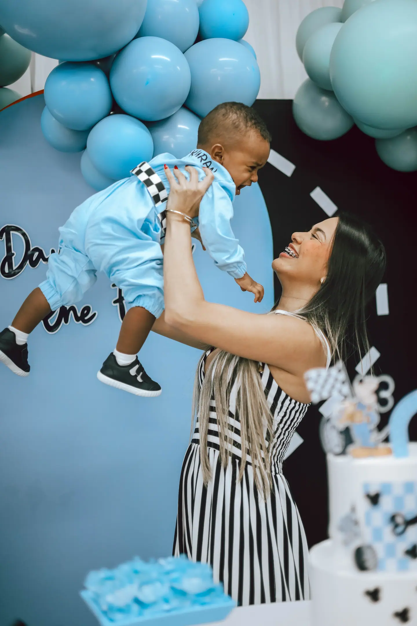 Mãe lança o filho para o alto diante do painel de balões azuis