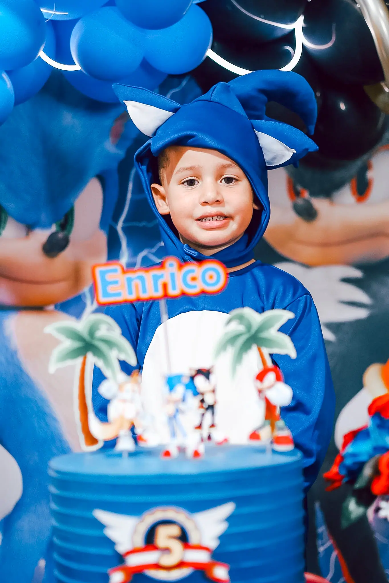 Menino de capuz do Sonic atrás do bolo de aniversário de cinco anos