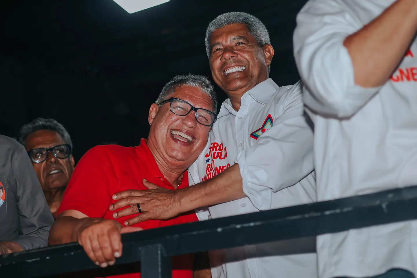 Dois homens gargalham debruçados no gradil do palco à noite