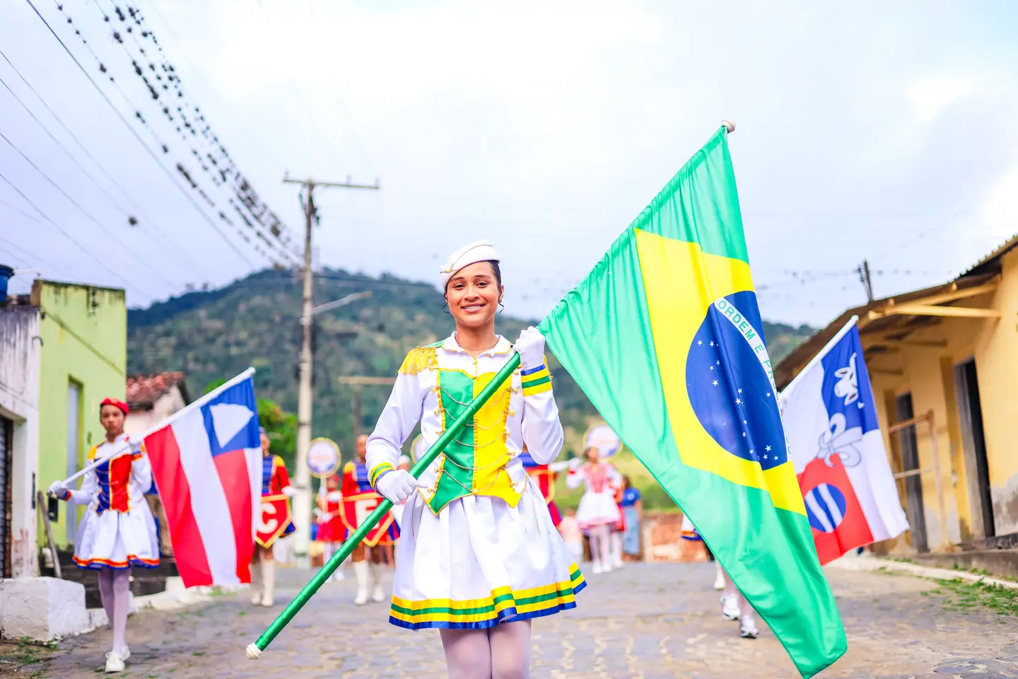 Balizadora desfila com a bandeira do Brasil em rua de casario