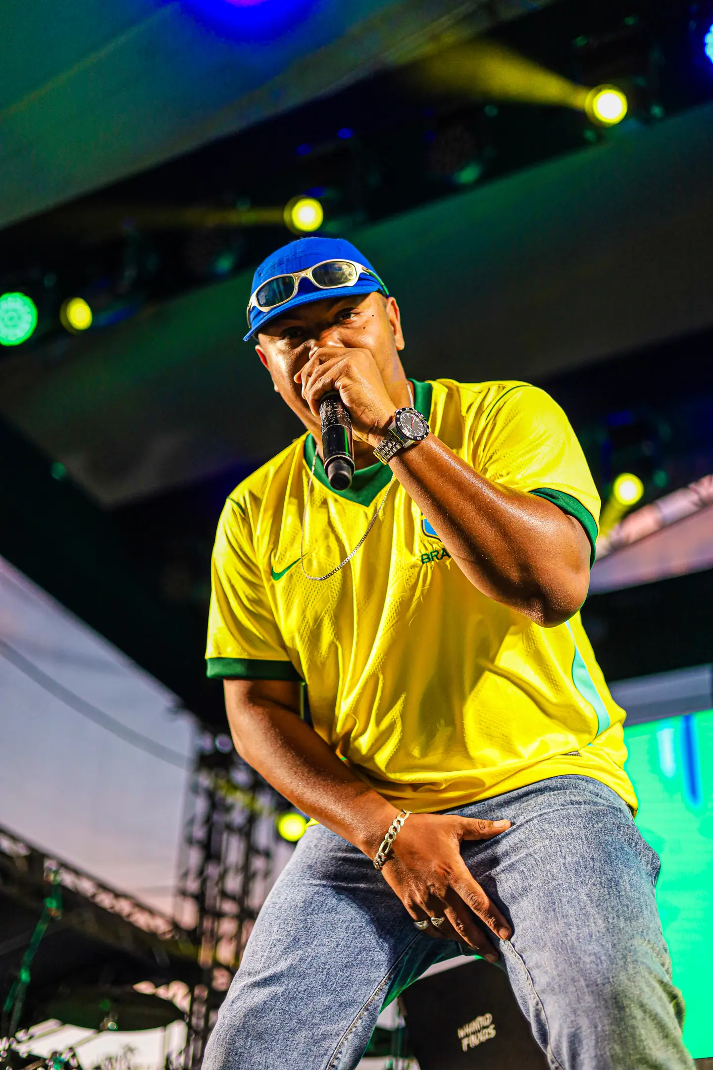 Rapper de camisa da seleção agachado na beira do palco